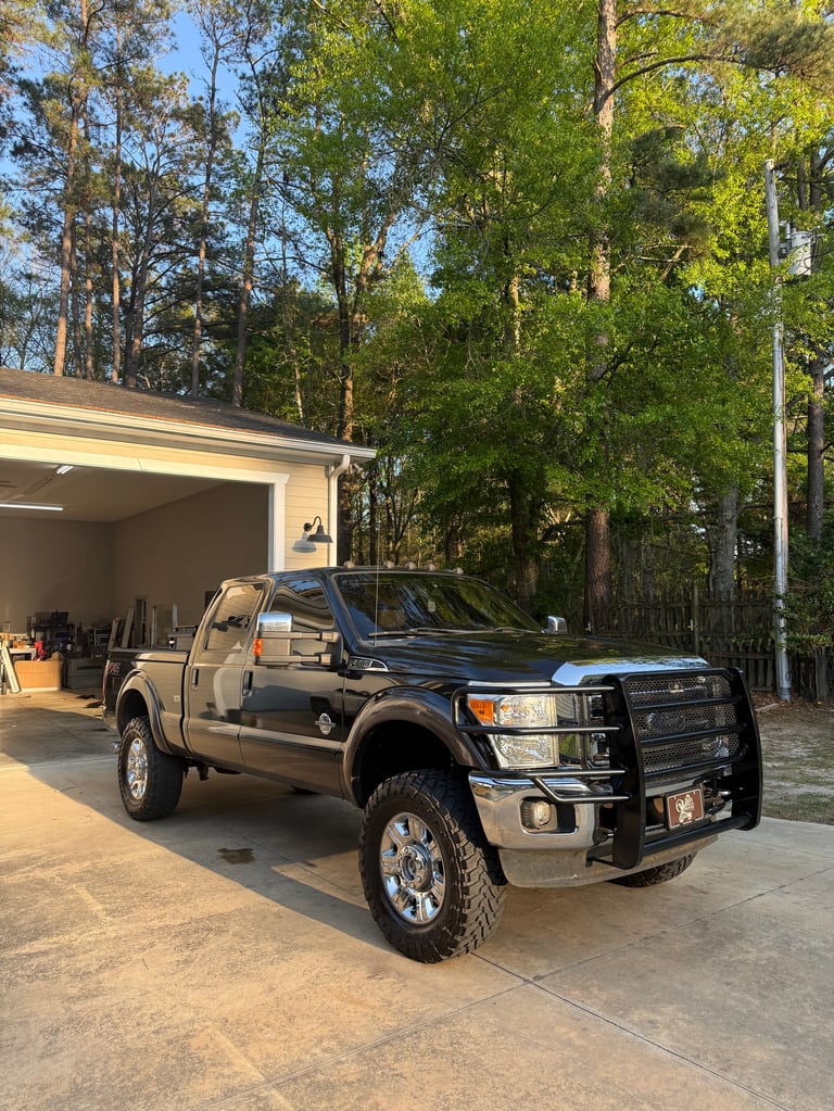 Black Ford pickup truck parked in driveway next to garage with pine trees in background
