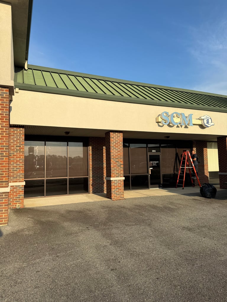 Empty storefront with brick facade, green metal roof, cream-colored awning, and a red ladder in the entrance under blue sky