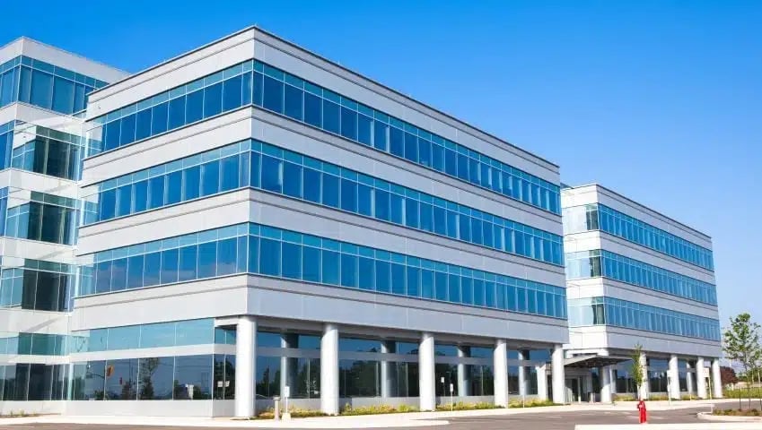 Modern multi-story office building with white and glass facade, featuring horizontal bands of windows against a clear blue sky