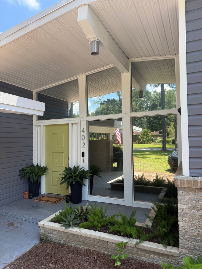 Modern home entrance with lime green door, large windows, covered porch, potted plants, and landscaping on sunny day