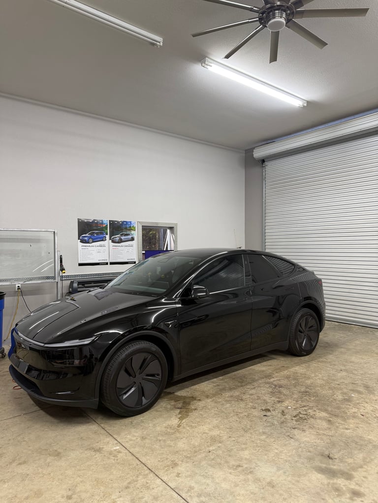 Black electric SUV parked in a garage with concrete floor, overhead lighting, and a rolling door.