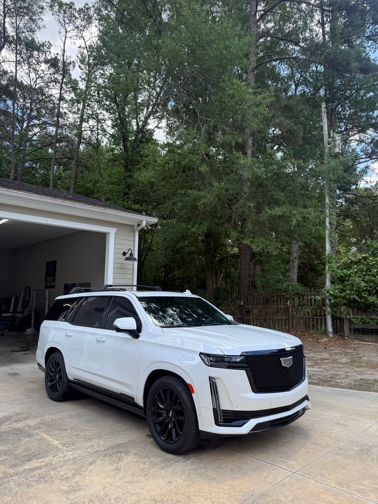 White Cadillac Escalade SUV parked in driveway in front of garage and tall trees