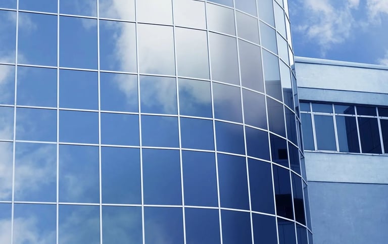 Modern curved glass building facade with grid pattern reflecting blue sky and clouds