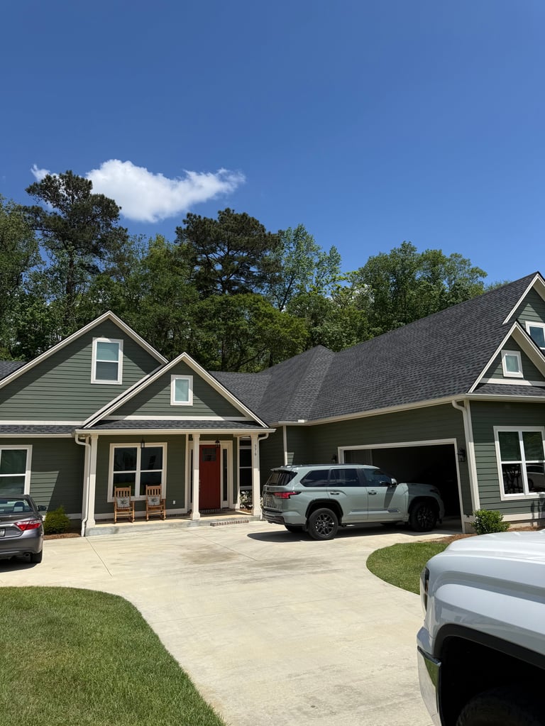 Modern two-story house with gray siding, attached garage, and white SUV parked in driveway on a sunny day with blue sky and trees